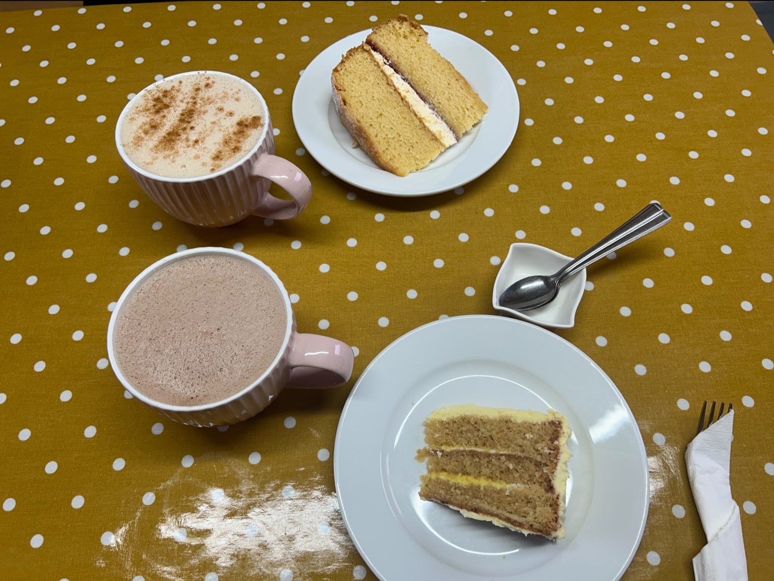 Two hot drinks and two slices of layered cake on a spotted tablecloth