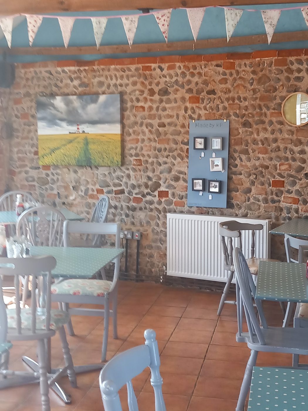Tables and chairs by a flint and brick wall with bunting